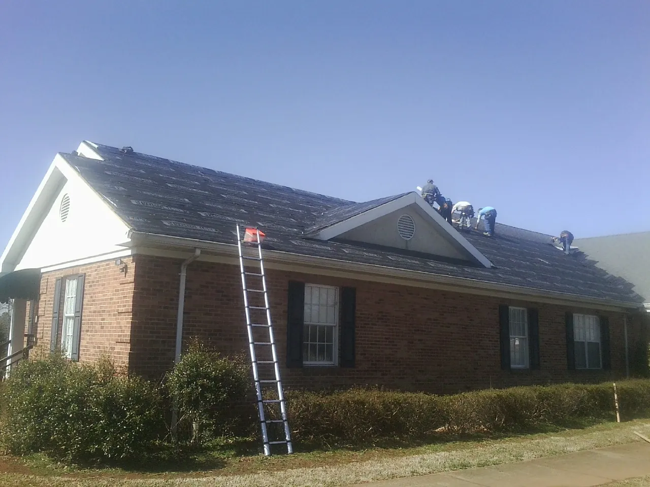 Crew tearing shingles off a brick ranch roof with a ladder set — Emergency Roof Repair work by our crew in Bradley