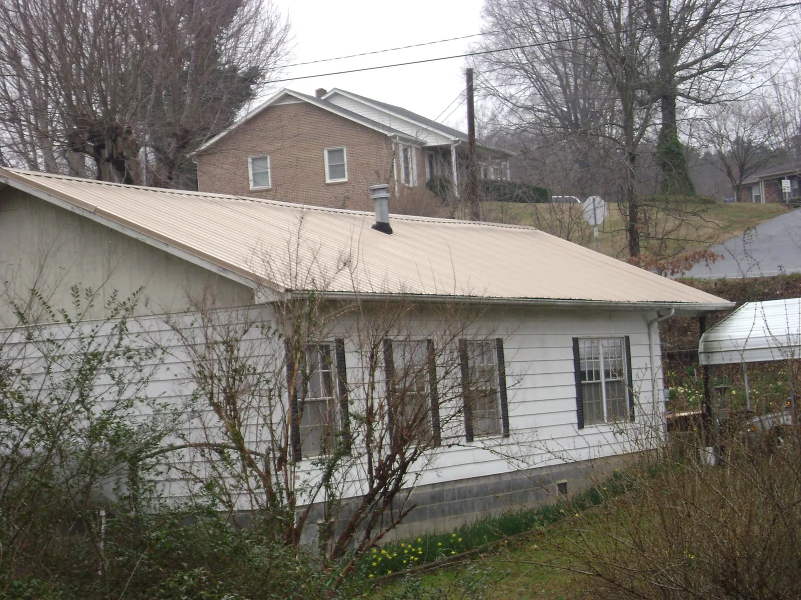 Tan metal roof on a white sided house set into a hillside — Commercial Roofing by Roofing Brothers in Bradley